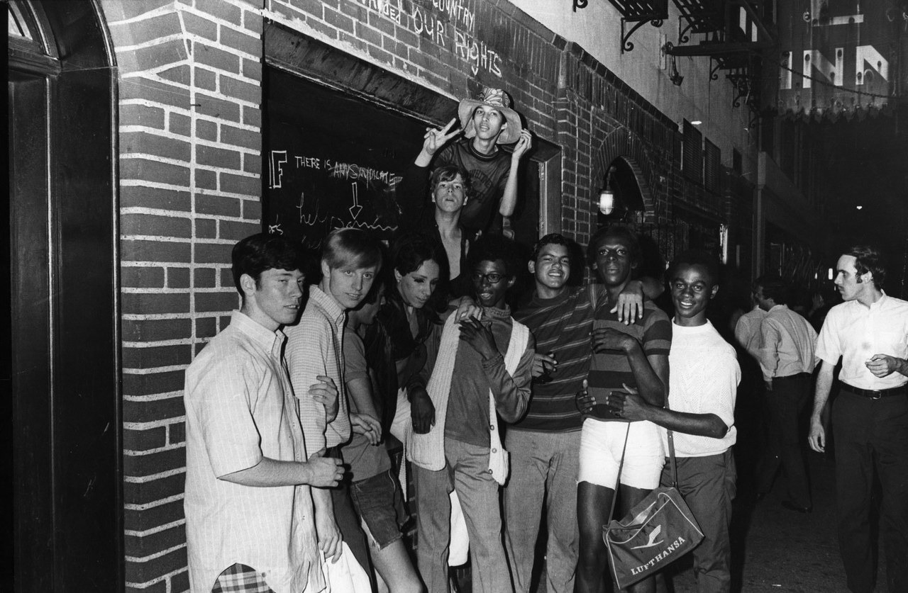 Black and white photo of young people outside the boarded-up Stonewall Inn after riots over the weekend of June 27, 1969.