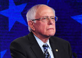 Bernie Sanders from the chest up, wearing a black suite and blue tie.