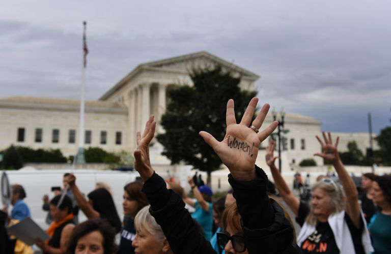 A group of anti-Kavanaugh protesters with their hands up walking in front of the Supreme Court. The hands in the middle have the word 